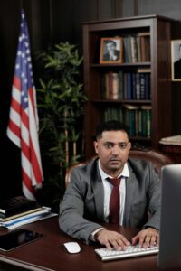 Professional Middle Eastern man working at office desk with American flag in background.